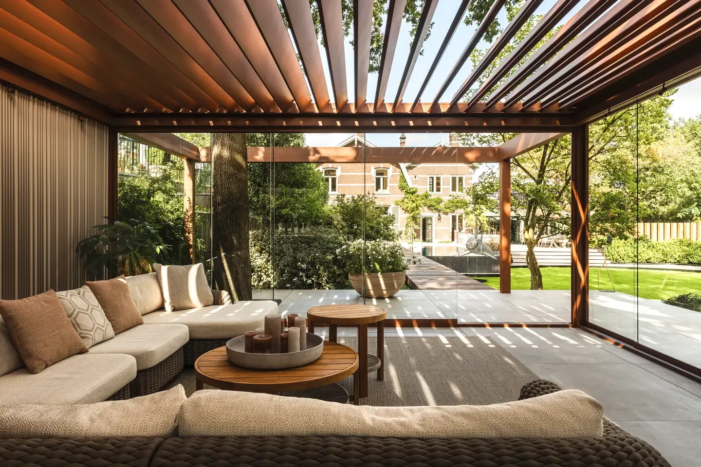 Bioklimatická pergola Renson od PLAS.cz s prosklenými stěnami a moderním venkovním posezením, která majitele chrání před nepříznivým počasím.