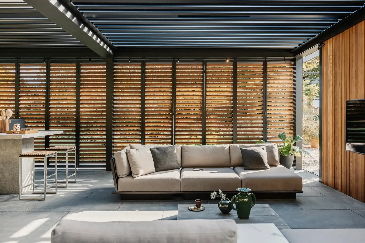 Bioklimatická pergola Renson od PLAS.cz s nastavitelnou střešní clonou a bočním stíněním, která vytváří komfortní venkovní jídelní kout.