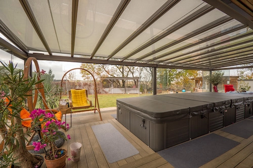 Nezateplená prosklená pergola od PLAS.cz s vířivkou a relaxačním posezením, ideální pro odpočinek v jakémkoli ročním období.