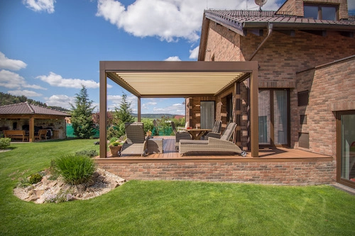 Bioklimatická pergola Renson od PLAS.cz elegantně ladící s cihlovým domem, která poskytuje stín a komfortní posezení na terase.