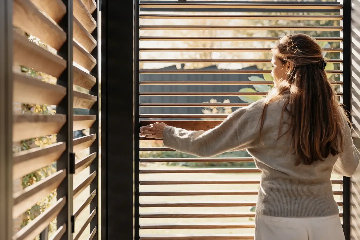 Bioklimatická pergola Renson od PLAS.cz s červenými lamelami a prosklenými stěnami, která vytváří elegantní venkovní posezení na terase s výhledem na město.