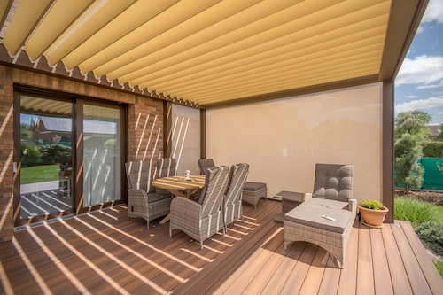 Bioklimatická pergola Renson od PLAS.cz s nastavitelnou střešní clonou a bočním stíněním, která vytváří komfortní venkovní jídelní kout.